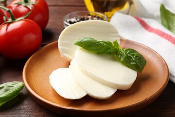 Tasty mozzarella, tomatoes and basil on wooden table, closeup