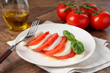 Tasty mozzarella, tomatoes, oil and basil on wooden table, closeup