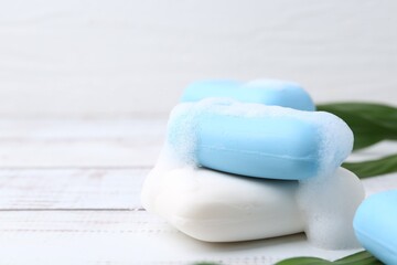 Soap bars with foam on white wooden table, closeup. Space for text