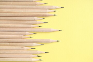 Many graphite pencils on yellow background, flat lay. Space for text