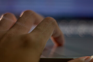 Close-up of a hand in motion while typing on a laptop, illuminated by blue light from the screen. A concept of work, technology, and speed