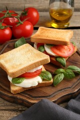 Tasty sandwiches with mozzarella cheese, tomatoes and basil on wooden table, closeup