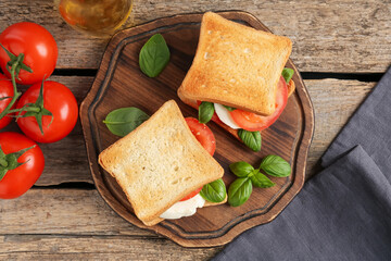 Tasty sandwiches with mozzarella cheese, tomatoes and basil on wooden table, flat lay