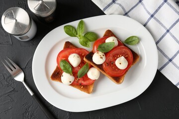 Tasty sandwiches with mozzarella cheese, tomatoes, basil and fork on dark textured table, flat lay