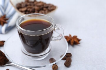 Cup of aromatic coffee, beans and star anise on white table, closeup. Space for text