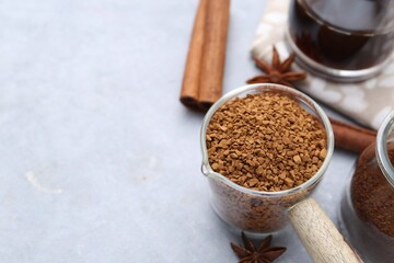 Granulated instant coffee in measuring cup and spices on grey table, closeup. Space for text