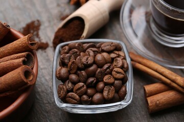 Roasted beans and cinnamon sticks on wooden table, closeup