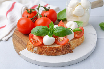 Tasty sandwich with mozzarella cheese, tomatoes and basil on light grey textured table, closeup