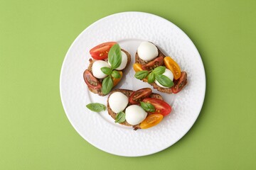Tasty sandwiches with mozzarella cheese, tomatoes and basil on green background, top view