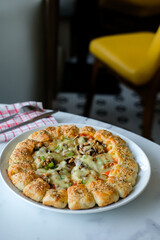 A circle of pizza on a plate with abundant cheese and toppings of vegetables and meat