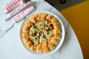 A circle of pizza on a plate with abundant cheese and toppings of vegetables and meat