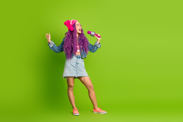 Energetic young woman with vibrant purple hair singing into microphone against a vibrant green background