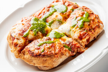 Close-up of a baked pizza slice with melted cheese, tomato sauce, and green pesto, served on a white plate. Crispy crust and vibrant toppings, isolated and appetizing.