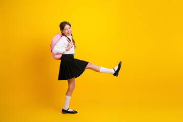 Energetic young student in a school uniform posing on a vibrant yellow background with a cheerful...