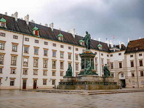 Innerer Burghof at Hofburg Palace, Vienna, Austria. A grand statue of Emperor Francis II stands amid historic architecture beneath a dramatic sky in this iconic courtyard.