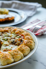 A circle of pizza on a plate with abundant cheese and toppings of vegetables and meat
