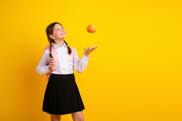 Happy schoolgirl tossing an apple against a bright yellow background, showcasing school spirit and academic enthusiasm.