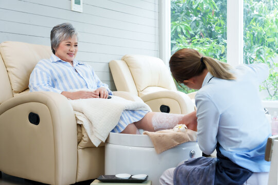 Spa technician providing foot care treatment to elderly woman at cozy nail spa salon ensuring personal grooming promoting relaxation wellness beauty lifestyle healthy hygiene in bright comfortable