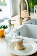 Plate with an ecobrush for washing dishes near the sink, soap in a glass bottle, a towel.