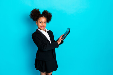 Confident schoolgirl in stylish uniform holding calculator against vibrant turquoise background, representing education and academic success