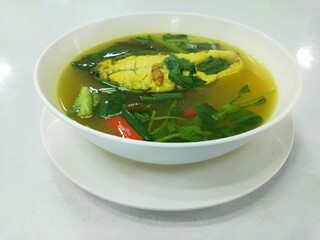 Thai turmeric fish soup in white bowl with herbs