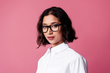 Stylish young woman sporting fashionable glasses against a vibrant pink backdrop
