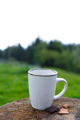 A Serene Coffee Moment: White Mug on a Rustic Wooden Surface Surrounded by Nature's Greenery and a Calm Background of Trees and Soft Overcast Sky for Relaxation