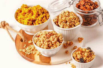 An assortment of granola varieties displayed in white bowls on a wooden board.