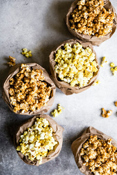An assortment of popcorn flavors in brown paper bags on a textured surface.