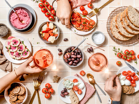 Overhead shot of women hands sharing a colorful Mediterranean brunch with fresh vegetables, bread, and drinks on a tiled table.jpg