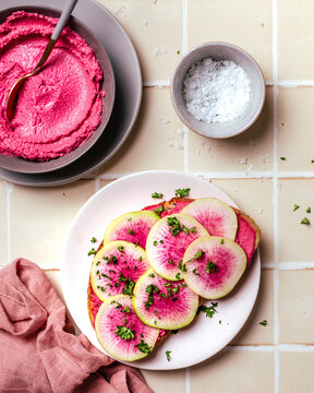 Overhead view of beet hummus toast topped with sliced watermelon radish on tiled surface.jpg