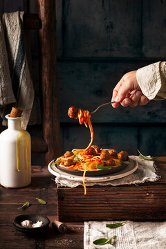 human hand holding fork with spaghetti and meatball