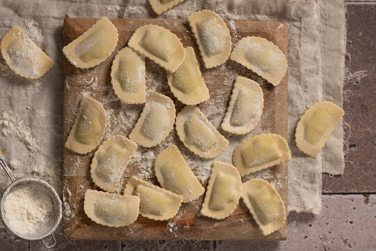 directly above home made ravioli on wooden cut board, with sifter and flour, ready to be cooked