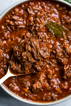 Close-up of a bowl of shredded beef stew with a rich tomato sauce and a bay leaf garnish.