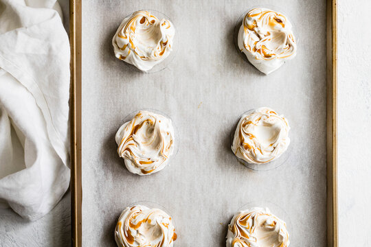 Six swirled meringue nests with caramel on a baking sheet lined with parchment paper.