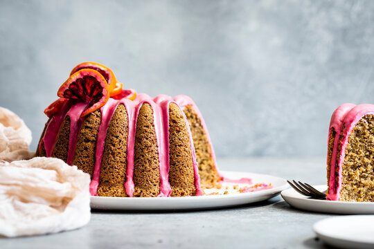 A bundt cake with vibrant pink icing and citrus decorations on a white plate.