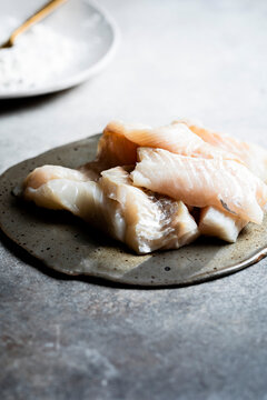 Raw fish fillets are placed on a rustic ceramic plate, ready for cooking.