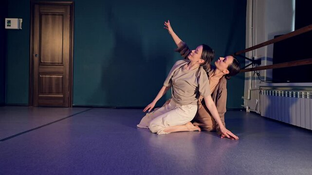 Two pretty Caucasian women in casual beige clothes are dancing in duet presenting modern ballet. The female pair demonstrates grace and agility through acrobatic moves and masterful choreography