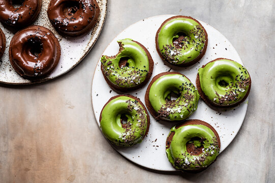 An assortment of chocolate and matcha glazed donuts on ceramic plates.