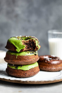 A stack of chocolate donuts with green icing and black sesame seeds, accompanied by a glass of milk.