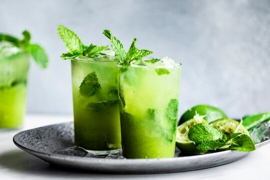 Two refreshing mojitos garnished with mint leaves and lime served on a tray.