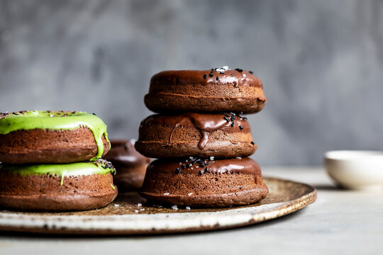 A plate of chocolate donuts with green and brown icing, garnished with seeds.