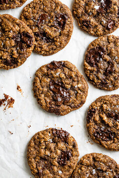 A batch of oatmeal chocolate chunk cookies with sea salt on parchment paper.