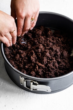Hands pressing a chocolate crumb crust into a springform pan.
