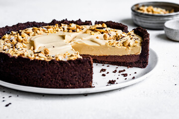 A sliced chocolate tart filled with creamy peanut butter topping and sprinkled with chopped peanuts on a white plate.