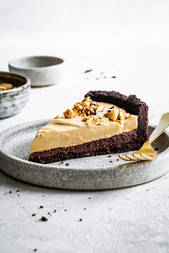 A slice of chocolate and peanut butter pie topped with chopped nuts on a patterned plate with a gold fork.