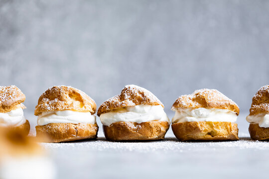 A row of cream-filled pastries dusted with powdered sugar on a light background.