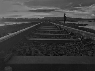 silhouette a man fishing in a lake beside the train tracks