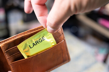A man's hand taking out a large-sized condom from a his wallet