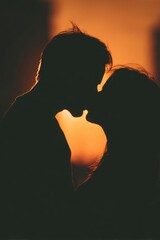 Silhouette of a couple kissing against a warm orangey sunset background